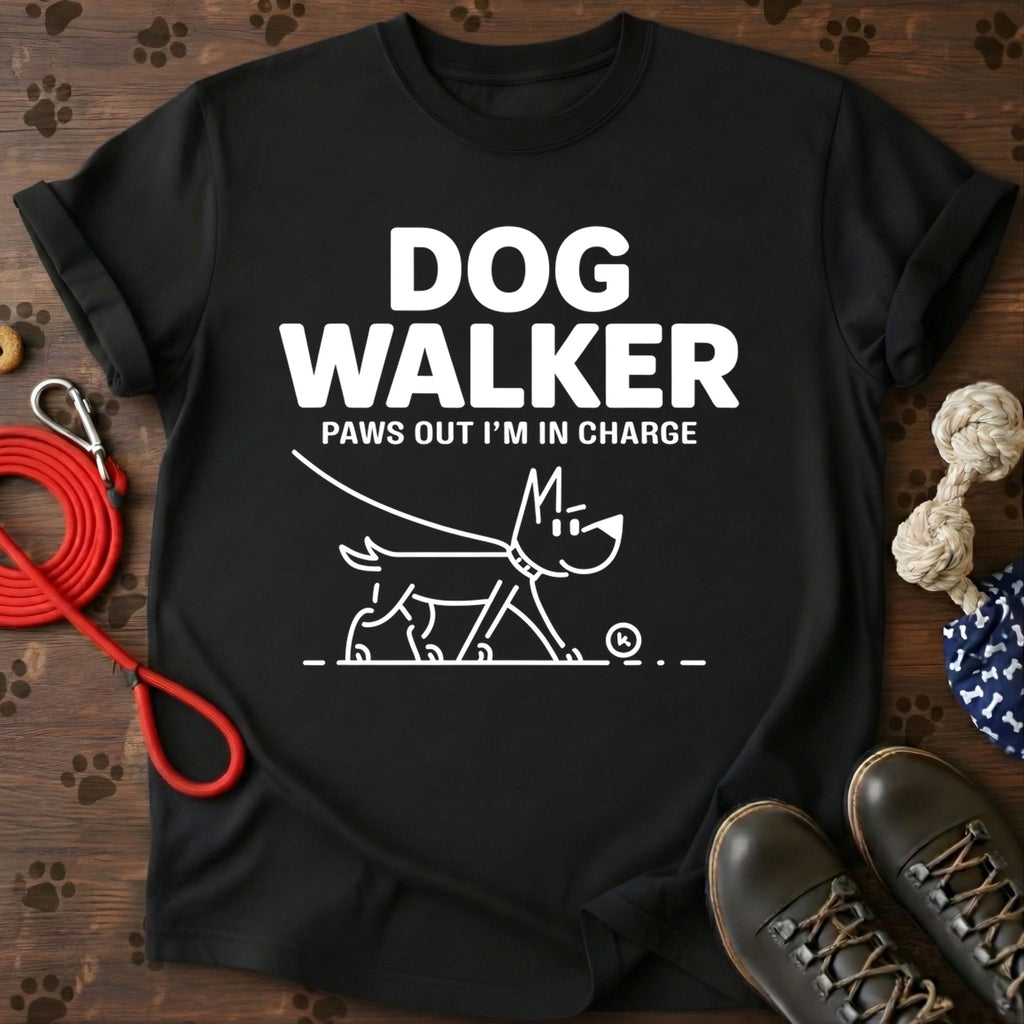 Black t-shirt with 'Dog Walker Paws Out I'm in Charge' text and graphic on a wooden surface with dog-related items.